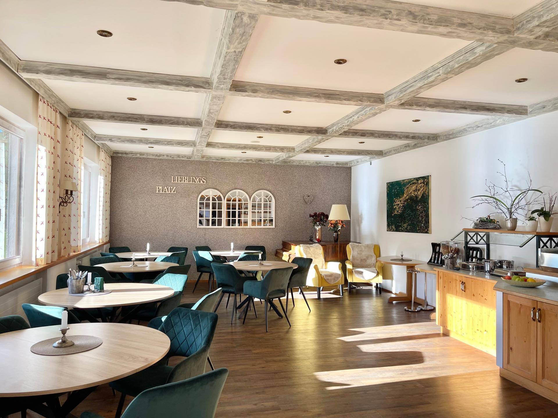 Heller Speisesaal mit großen Fenstern, Holzboden und grünen Samtstühlen.