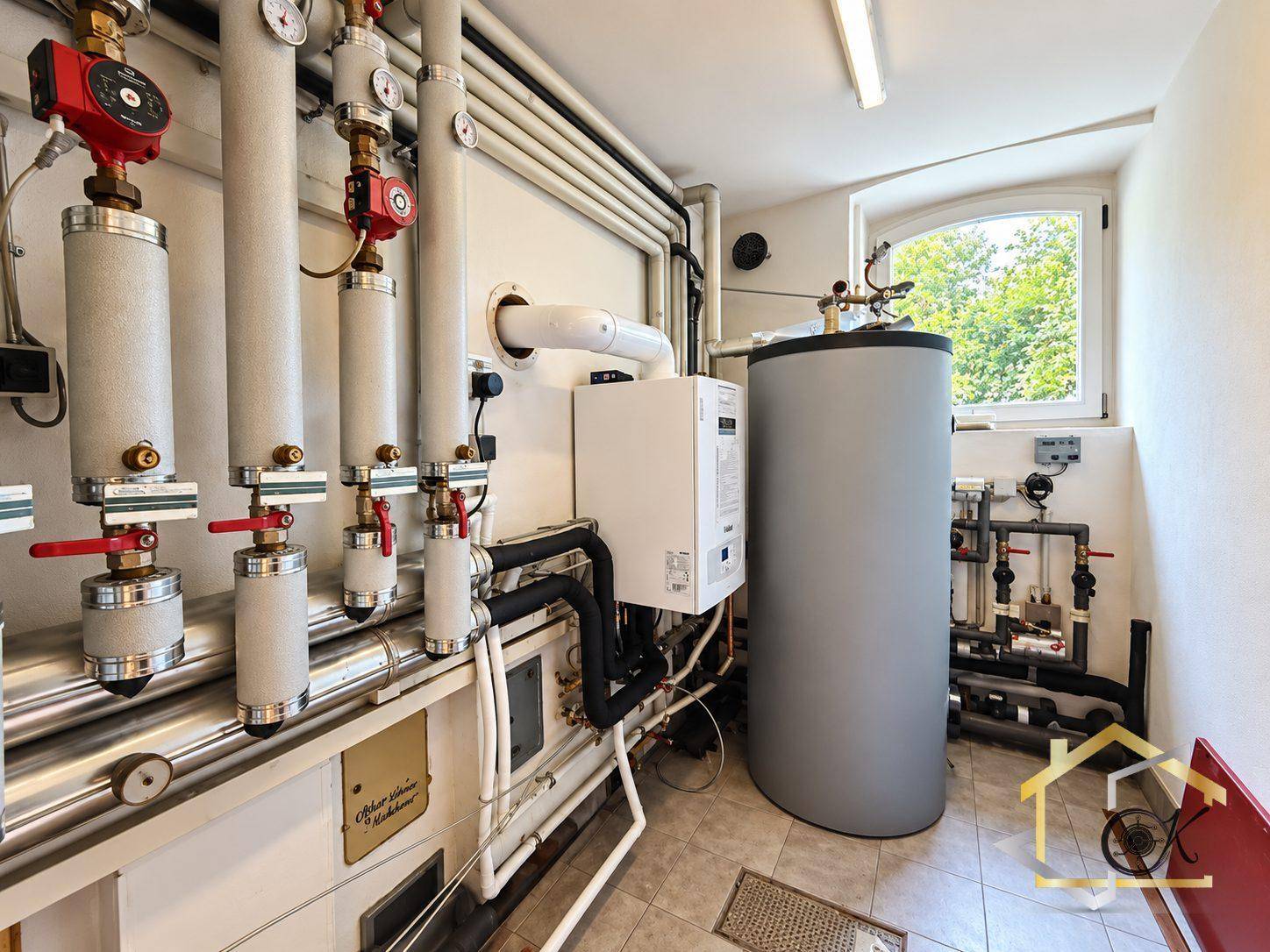 Heizungsraum mit moderner Heizungsanlage, Warmwasserspeicher und zahlreichen Leitungen.
