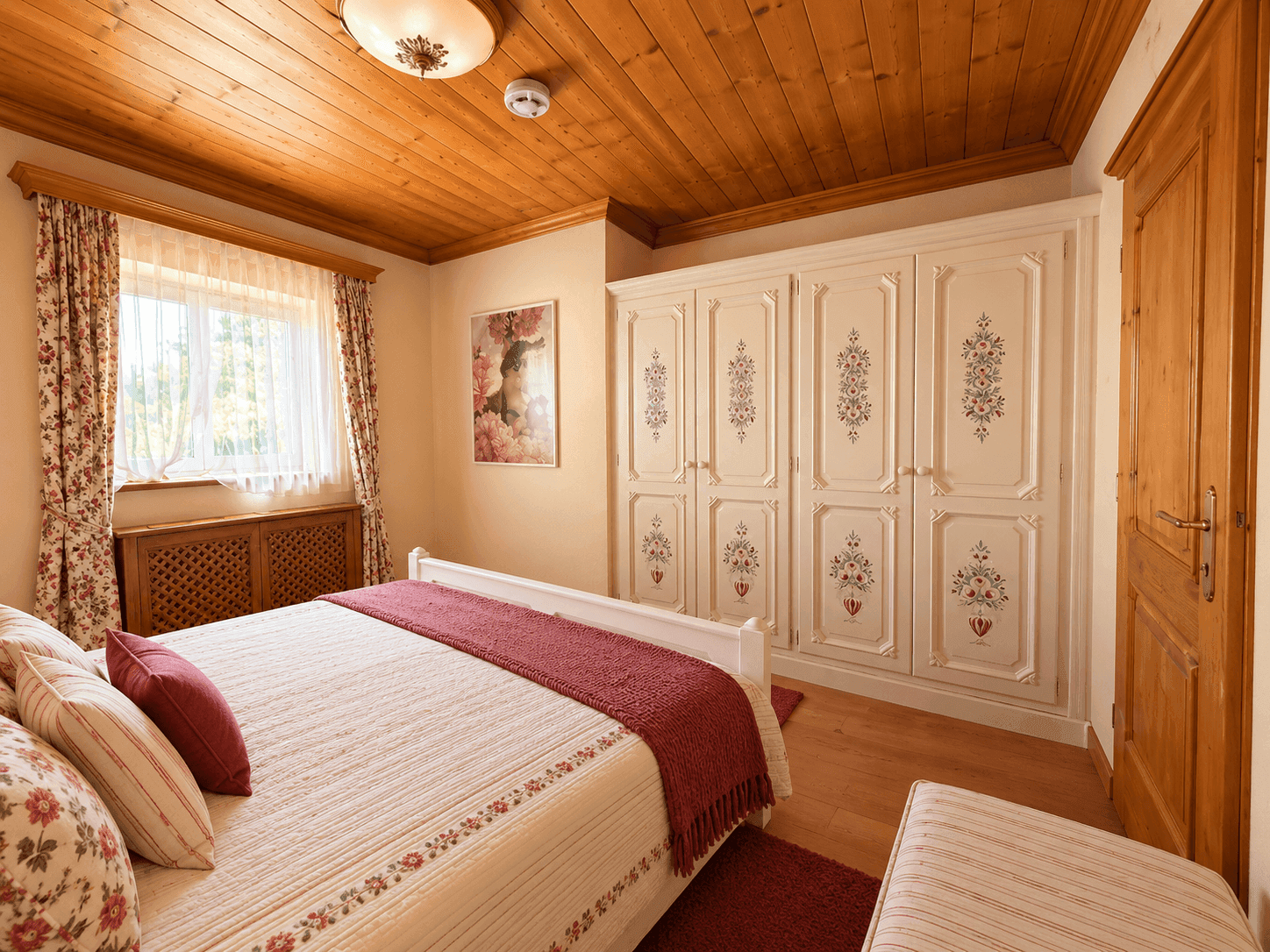 Gemütliches Schlafzimmer mit Holzbalkendecke, weißem Kleiderschrank und floralen Akzenten.