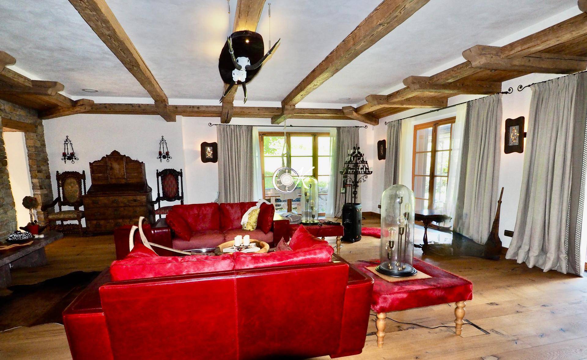 Geräumiges Wohnzimmer mit roten Sofas, Holzbalkendecke und großen Fenstern mit Blick ins Grüne.