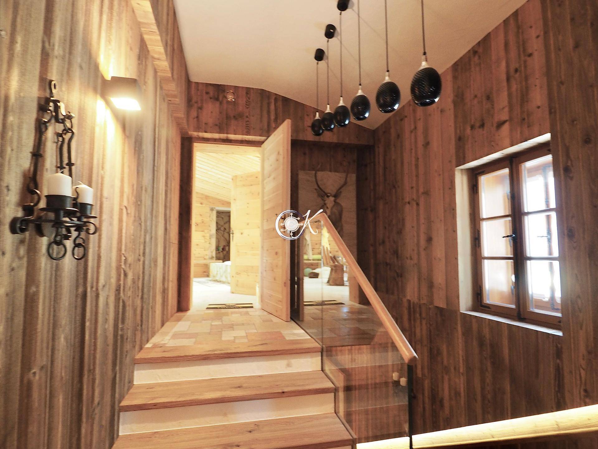 Rustikaler Flur mit Holzwänden, Holztreppe und moderner Beleuchtung.