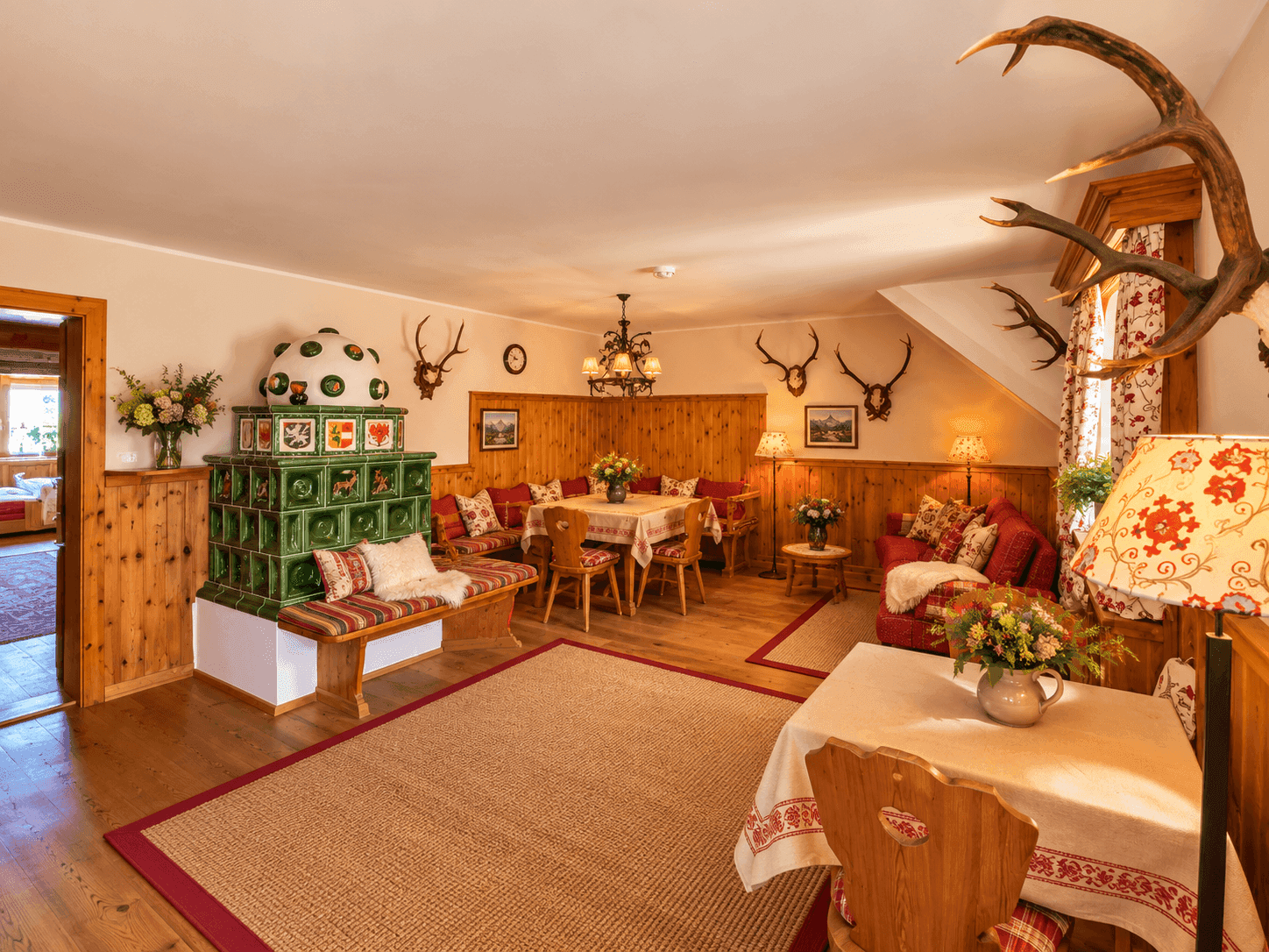 Geräumiger Wohn-Essbereich im alpinen Stil mit Kachelofen und Hirschgeweih-Dekoration.