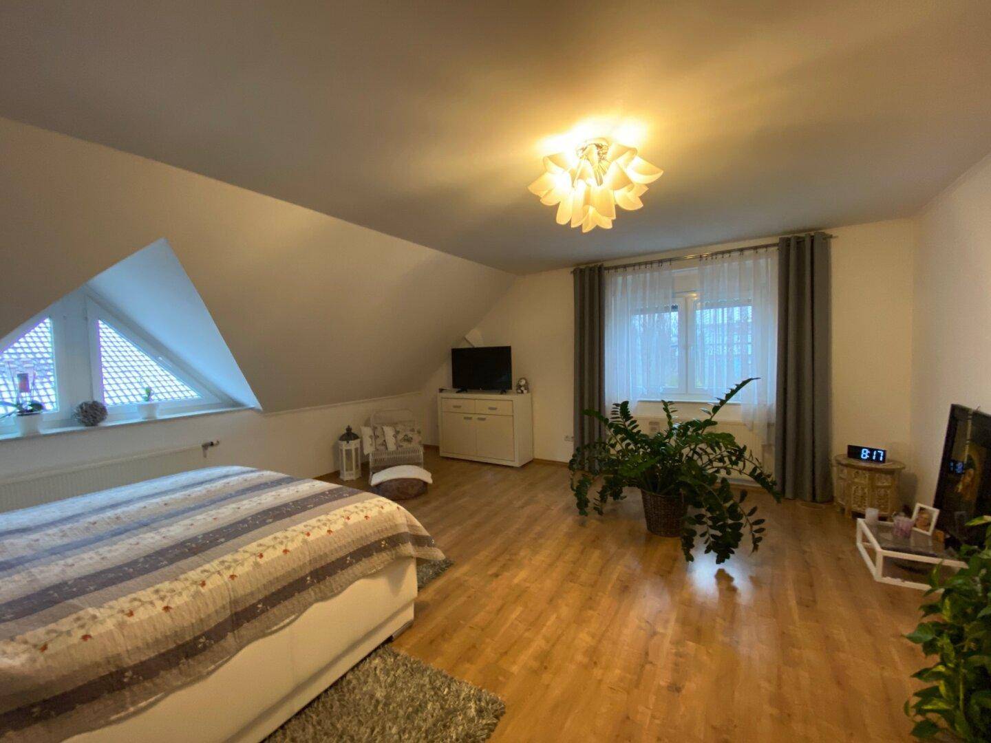 Geräumiges Schlafzimmer im Dachgeschoss mit Holzboden, schrägen Wänden und großem Fenster.