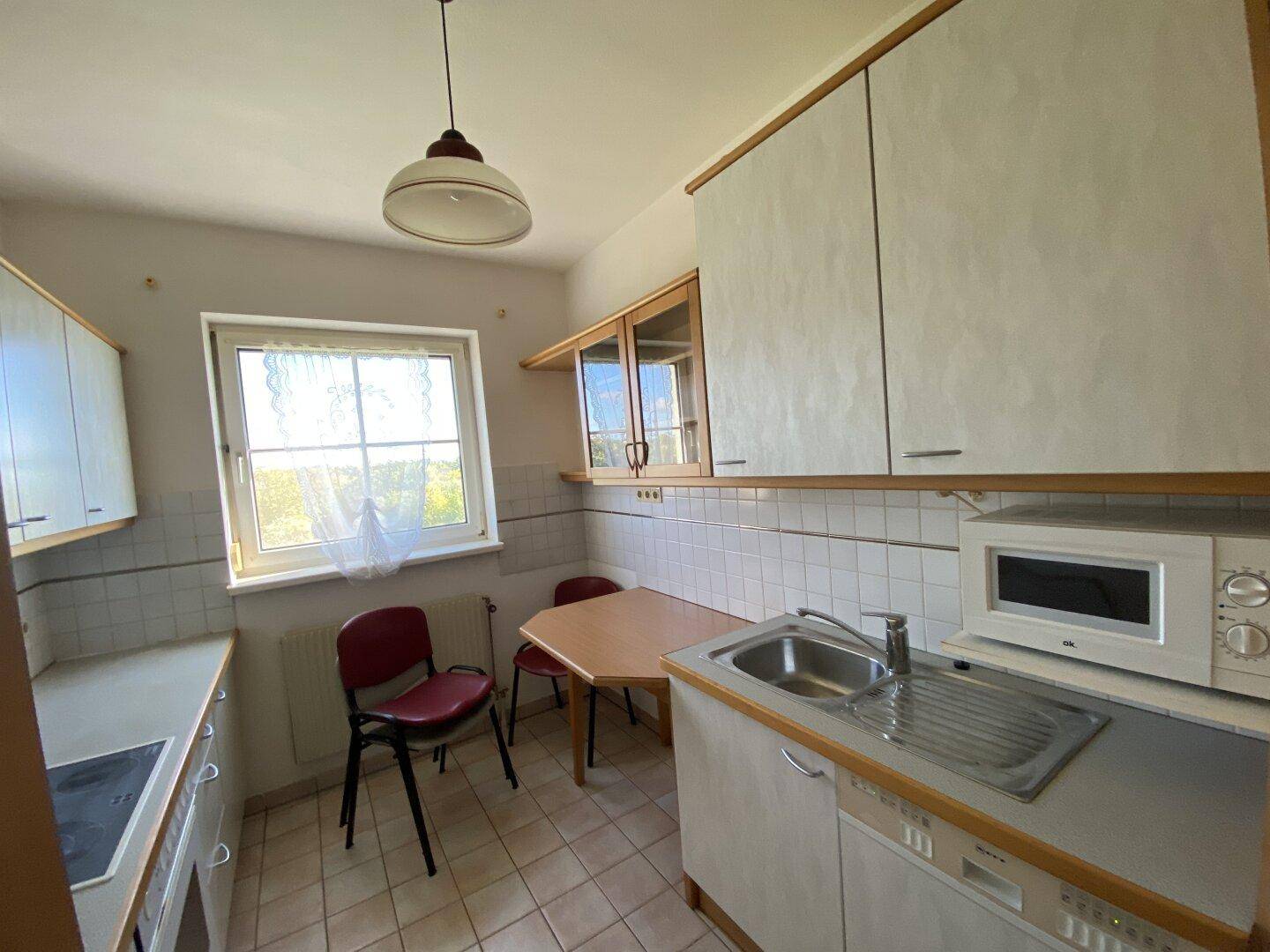 Funktionale Küche mit hellen Schränken, Spüle, Herd und einem kleinen Essbereich am Fenster.