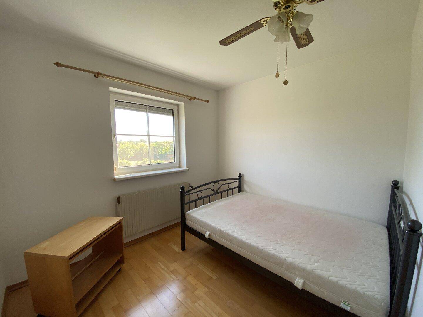 Gemütliches Schlafzimmer mit Einzelbett, Parkettboden, Fenster und Deckenventilator, hell und sauber.