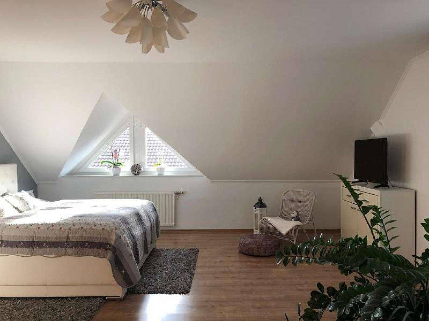 Helles Schlafzimmer im Dachgeschoss mit schrägen Wänden, Holzboden und großem Dreiecksfenster.