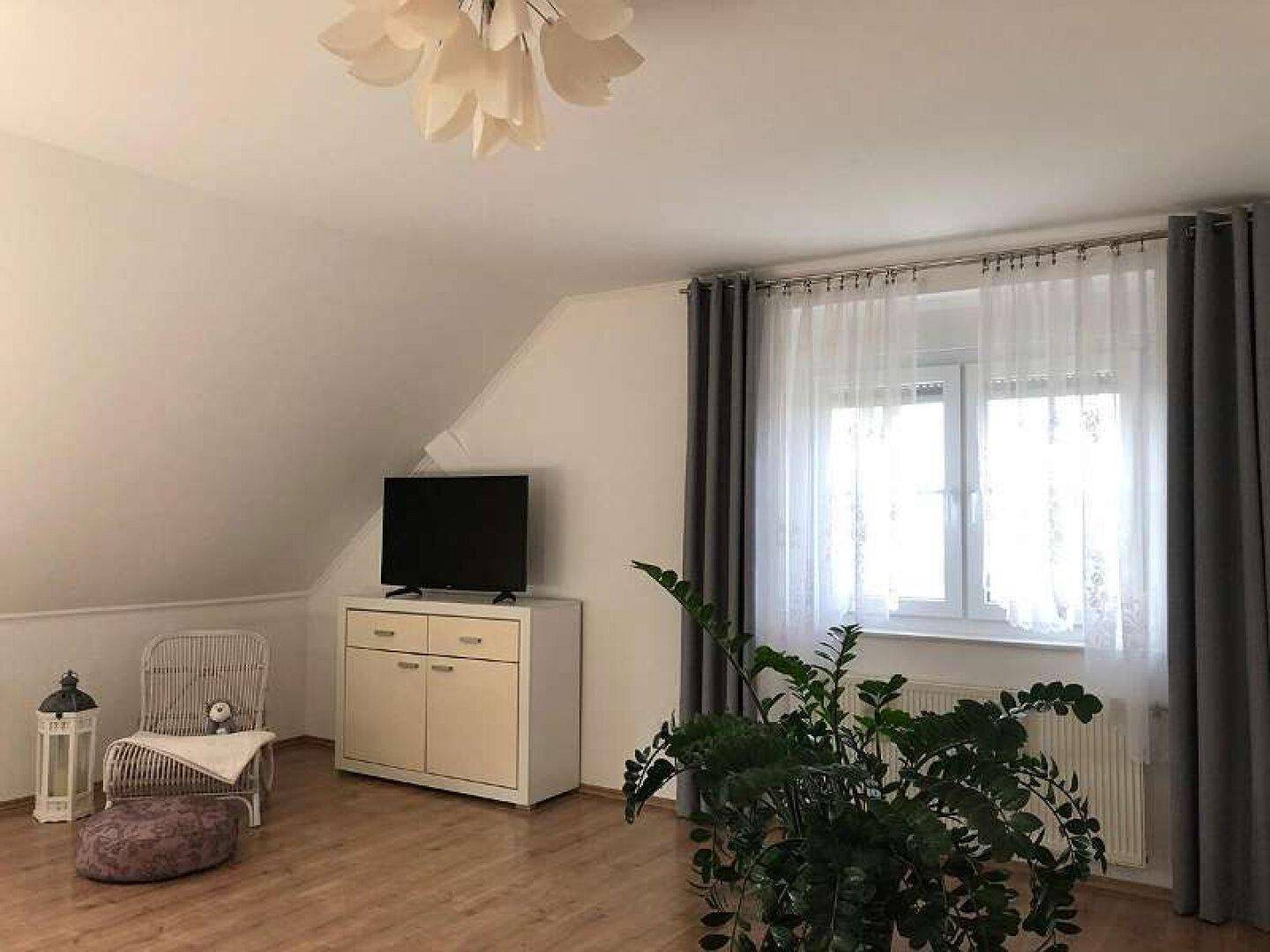 Gemütliches Schlafzimmer im Dachgeschoss mit Holzboden, schrägen Wänden und großem Fenster.