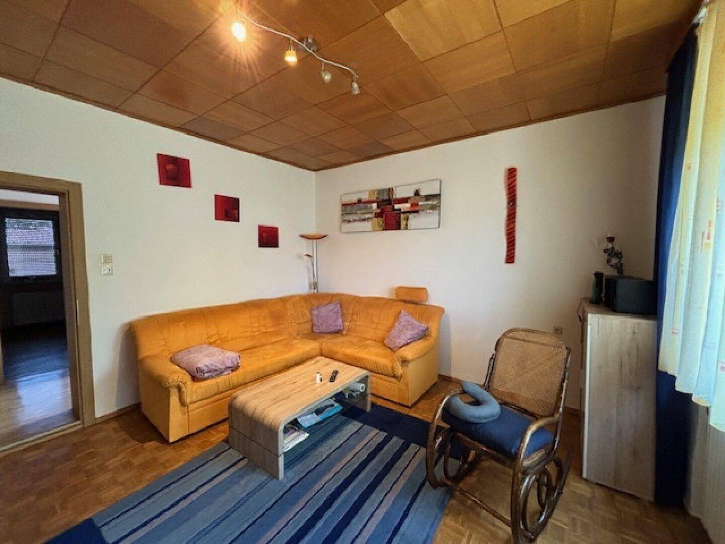 Gemütliches Wohnzimmer mit Ecksofa, Holztäfelung an der Decke und Parkettboden.