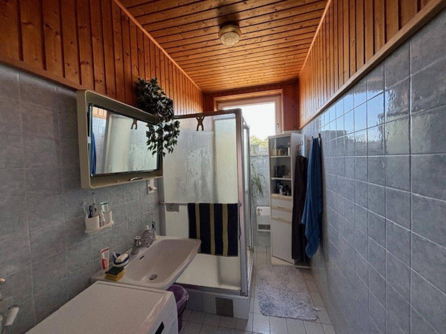 Badezimmer mit Duschkabine, Holzdecke und hellblauen Fliesen an den Wänden.