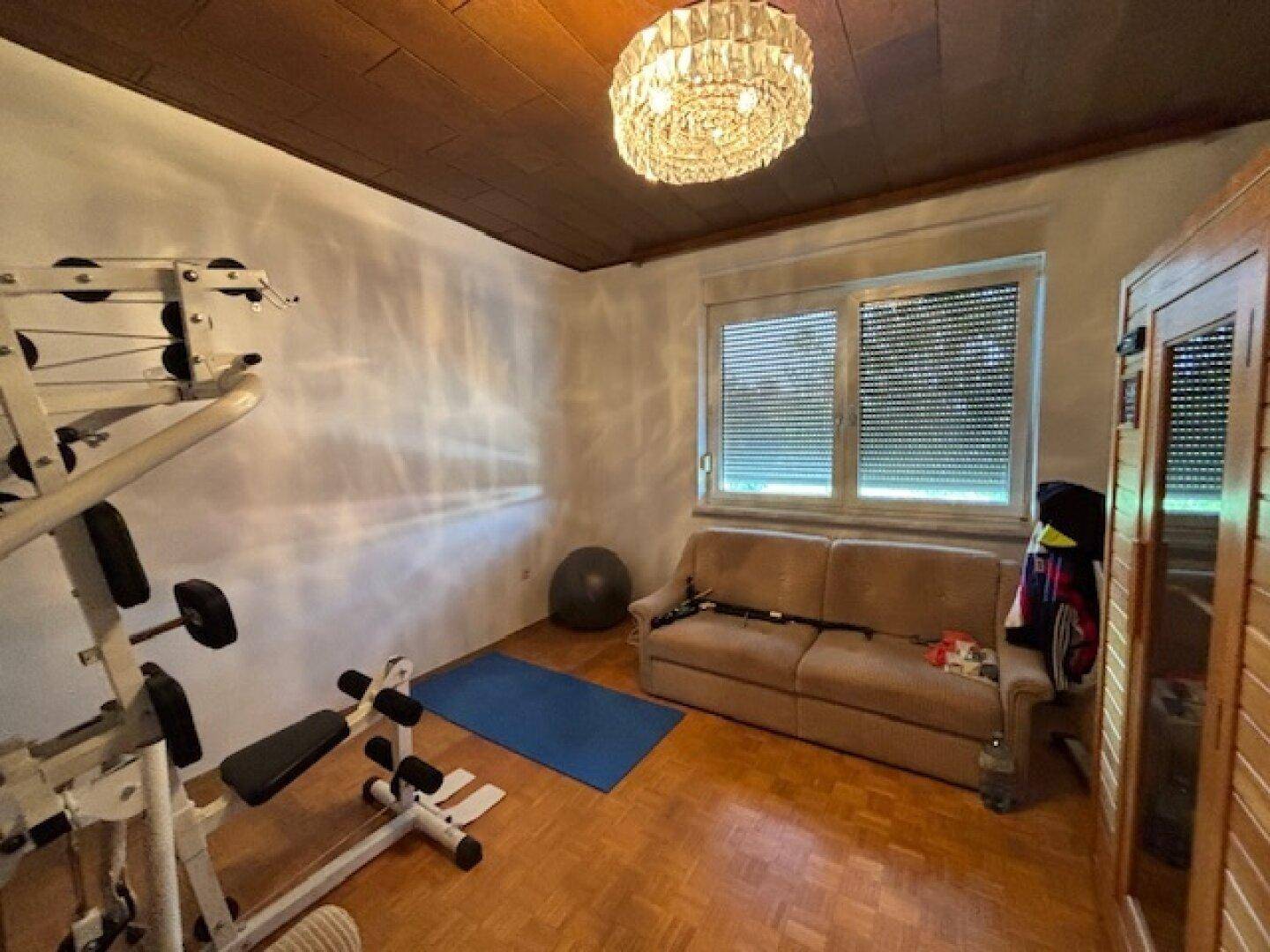 Raum mit Fitnessgeräten, Sofa und Holzdecke, ideal als Hobby- oder Arbeitszimmer.