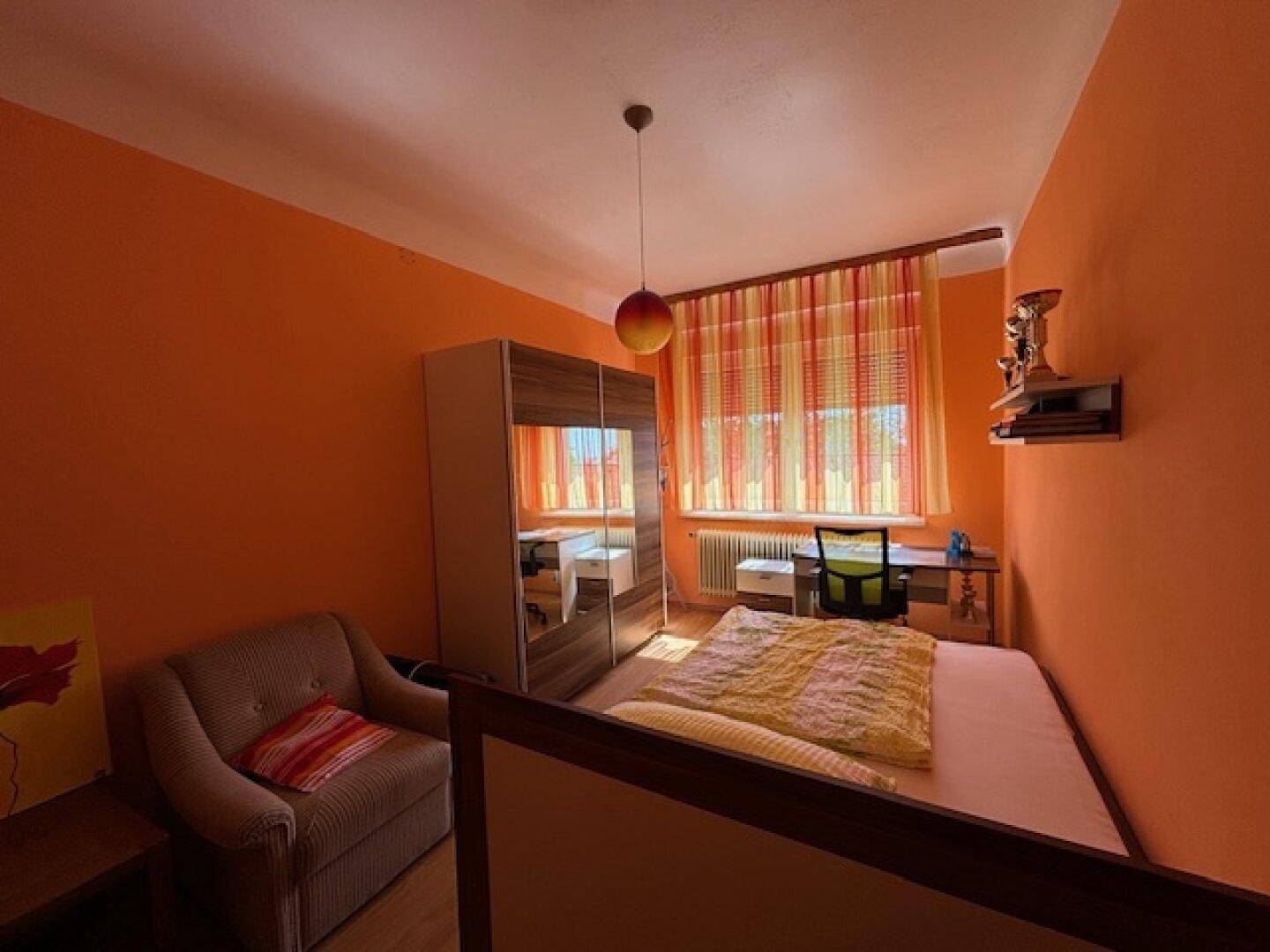 Schlafzimmer mit leuchtend orangefarbenen Wänden, Bett und Kleiderschrank mit Spiegeltür.