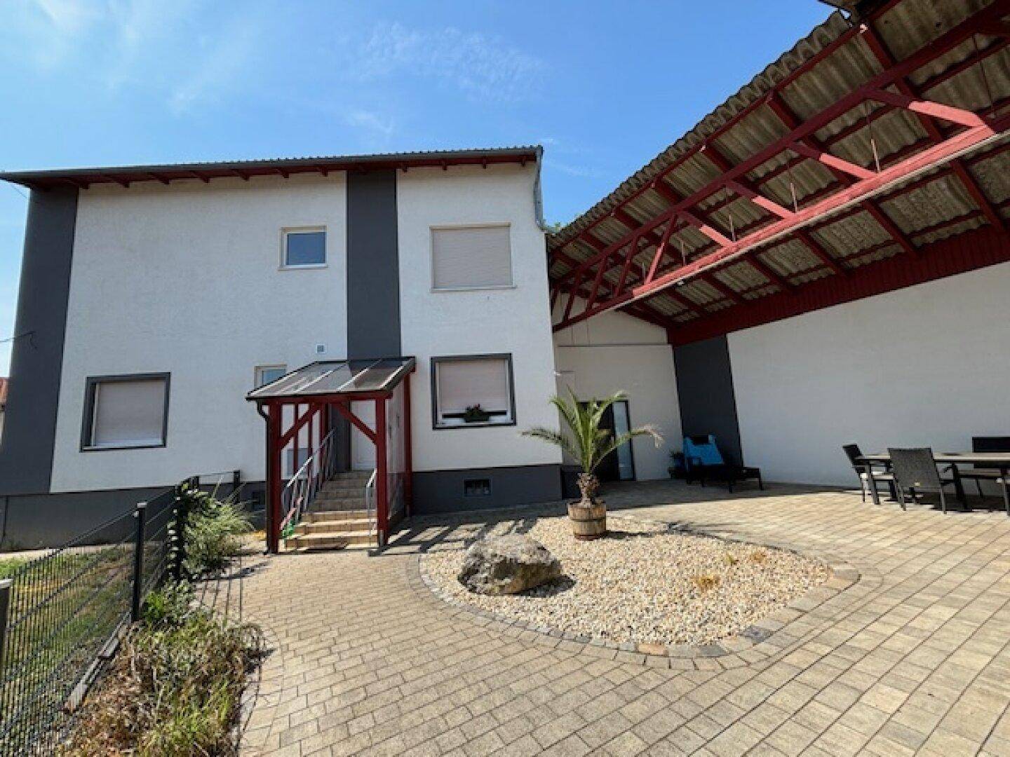 Hauptgebäude mit überdachtem Eingang und gepflastertem Innenhof mit Sitzgelegenheiten.