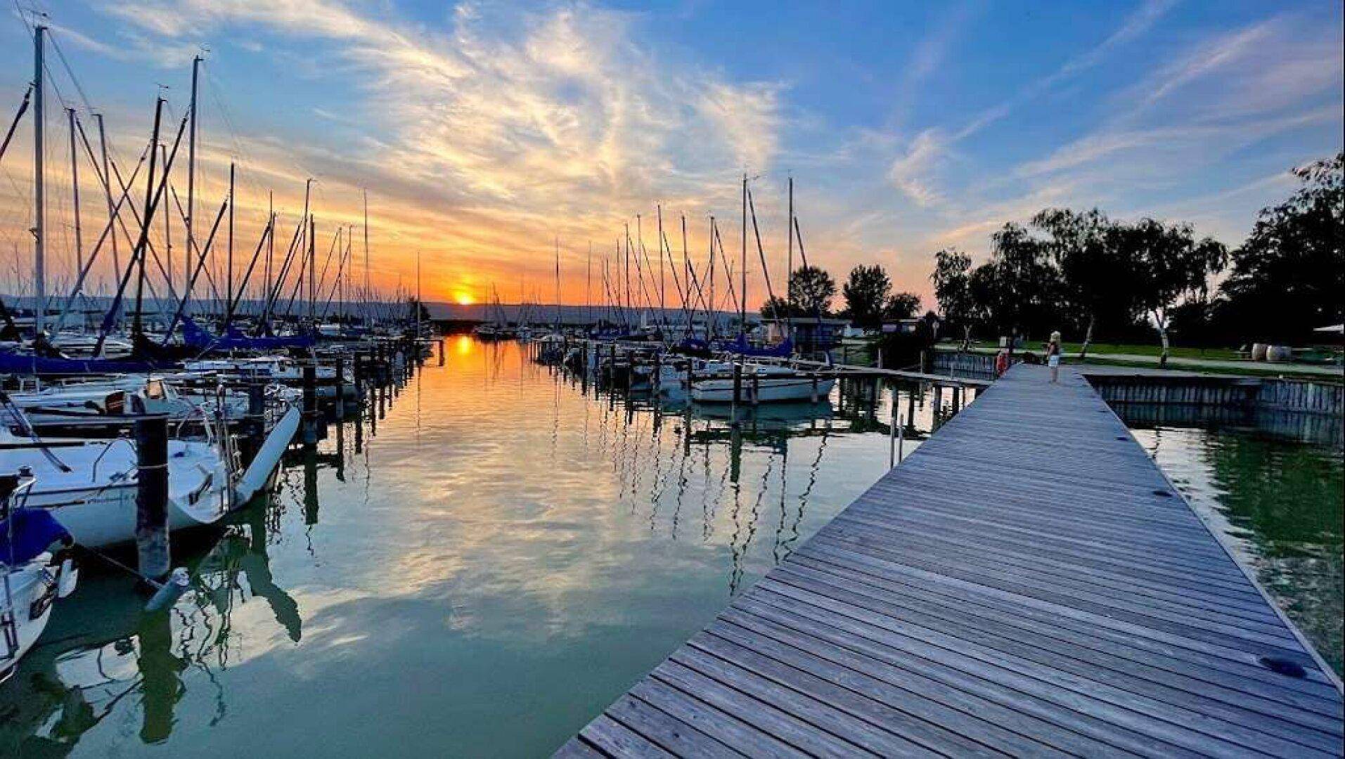 Malerischer Sonnenuntergang über einem Yachthafen mit zahlreichen Segelbooten und einem Holzsteg.