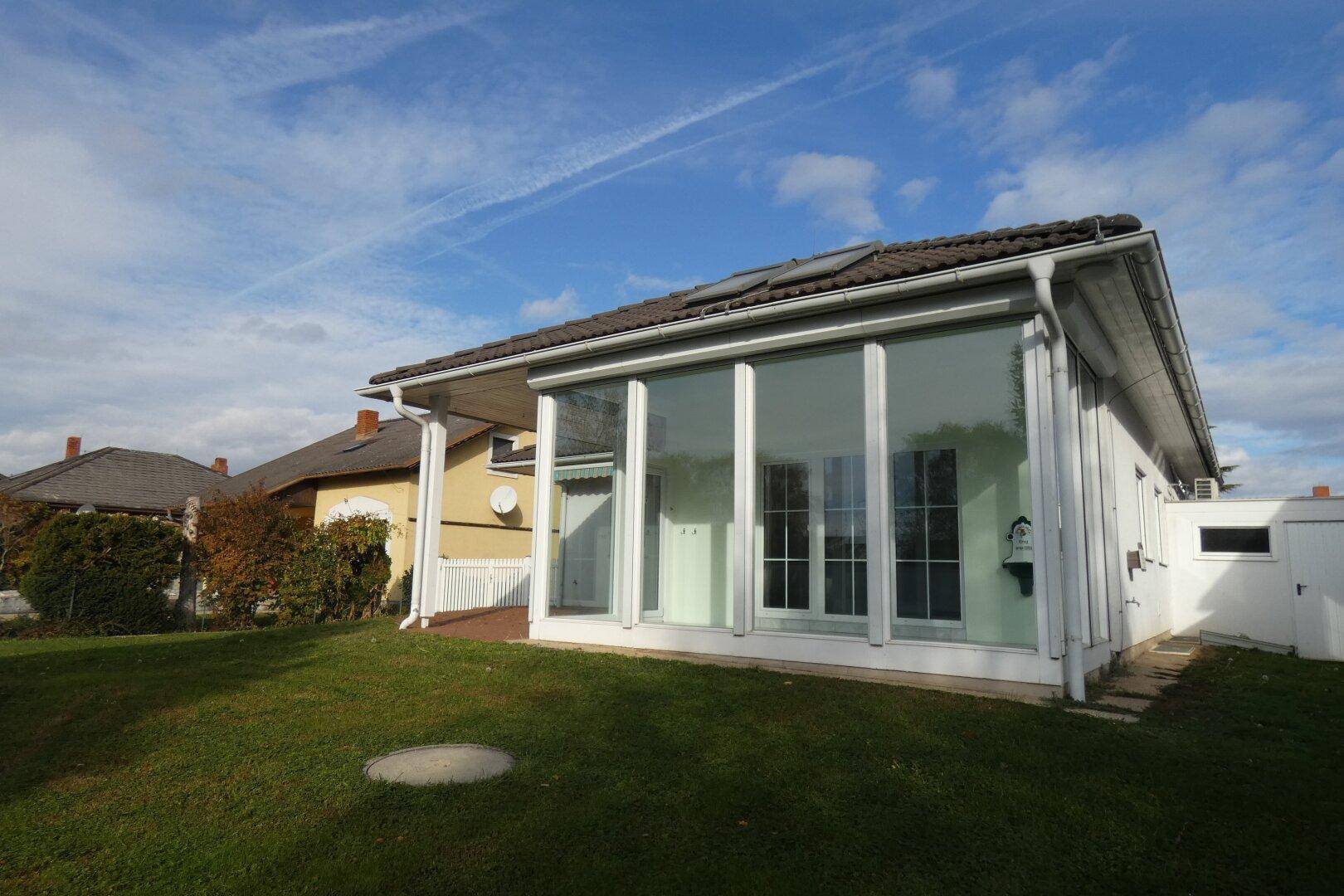 Rückansicht des Hauses mit großem Wintergarten und weitläufigem Gartenbereich.