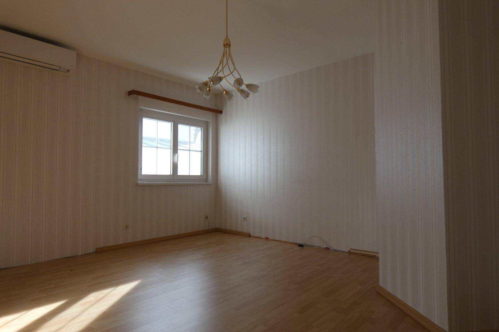 Leeres Zimmer mit gestreifter Tapete, Laminatboden und einem Fenster für natürliches Licht.