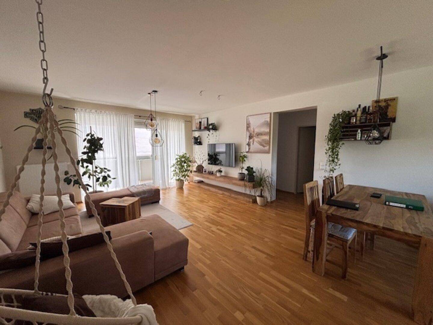 Geräumiger Wohnbereich mit bequemer Couch, Esstisch und Zugang zu einem Balkon durch große Fenster.