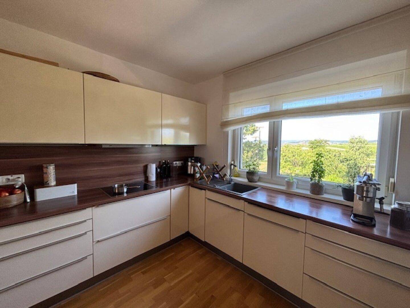 Moderne Küche mit hellen Schränken, Holzarbeitsplatten und einem großen Fenster mit Weitblick.