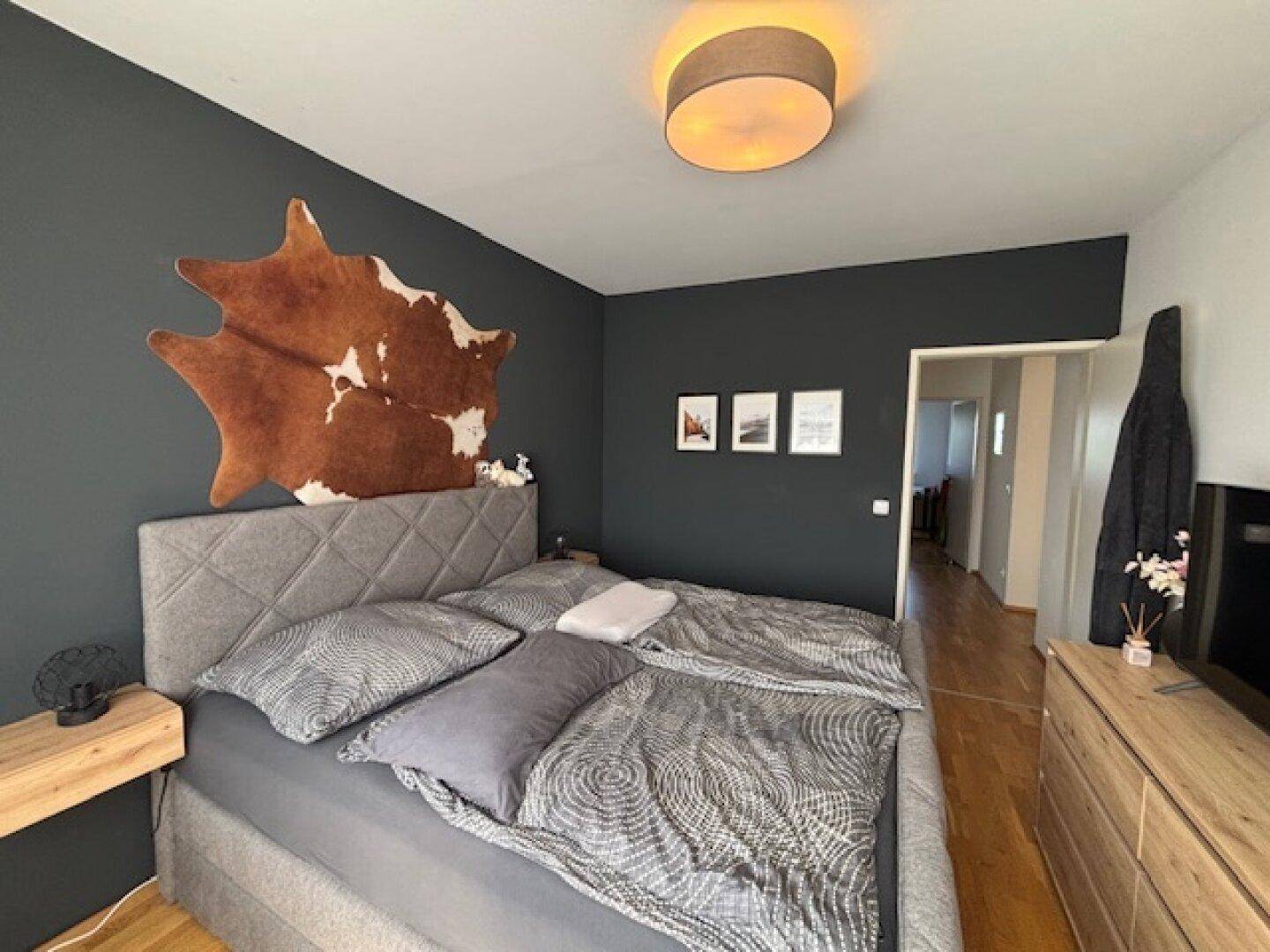 Schlafzimmer mit großem Bett, dunkler Akzentwand und Holzelementen, modern und gemütlich eingerichtet.