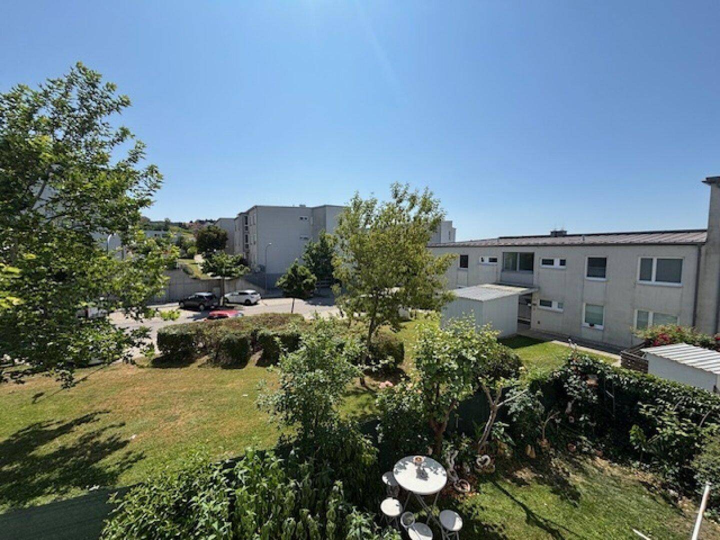 Blick auf den gepflegten Gemeinschaftsgarten mit Bäumen und Sitzgelegenheiten, umgeben von Wohngebäuden.