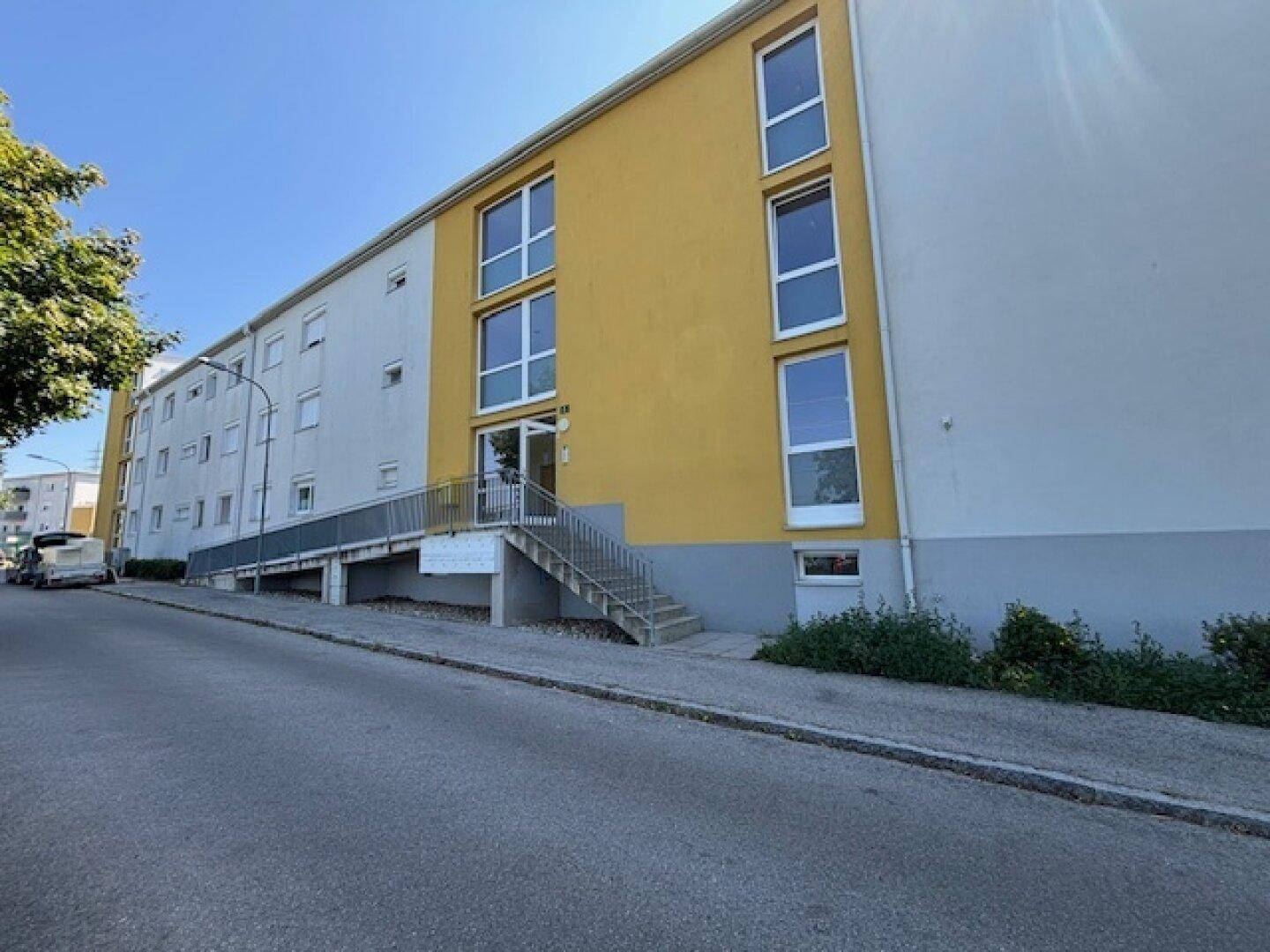 Moderne Gebäudefassade mit gelben und weißen Akzenten, inklusive Treppenzugang und Rampe.