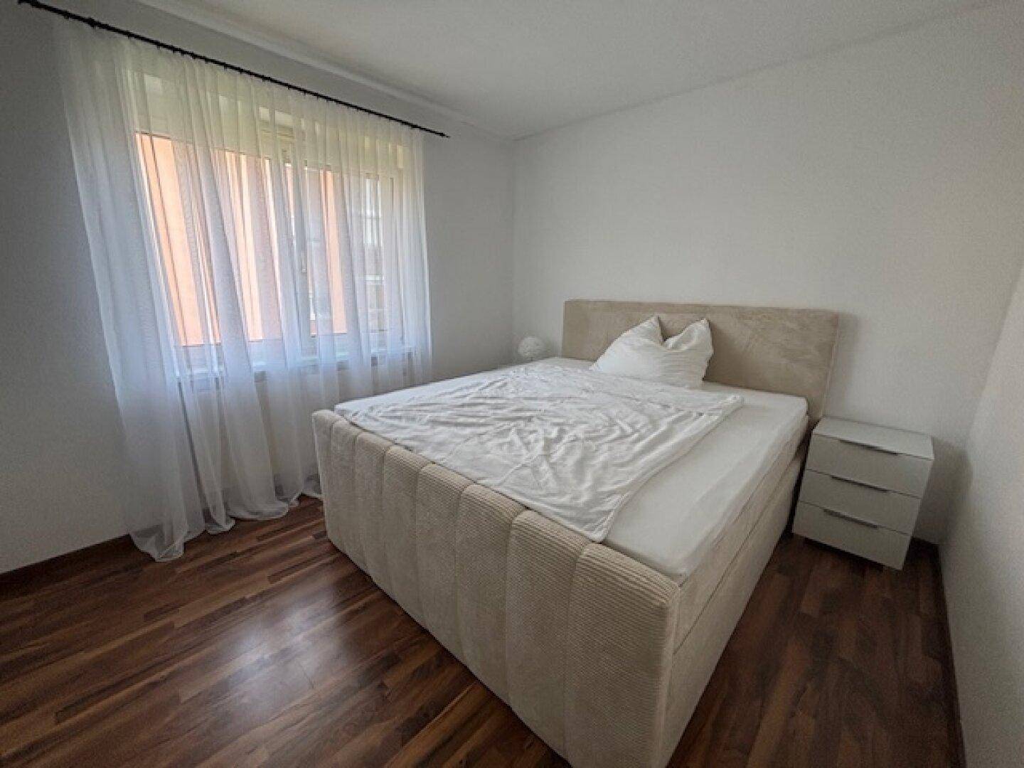 Schlafzimmer mit Doppelbett, Nachttisch und großem Fenster für viel Tageslicht.