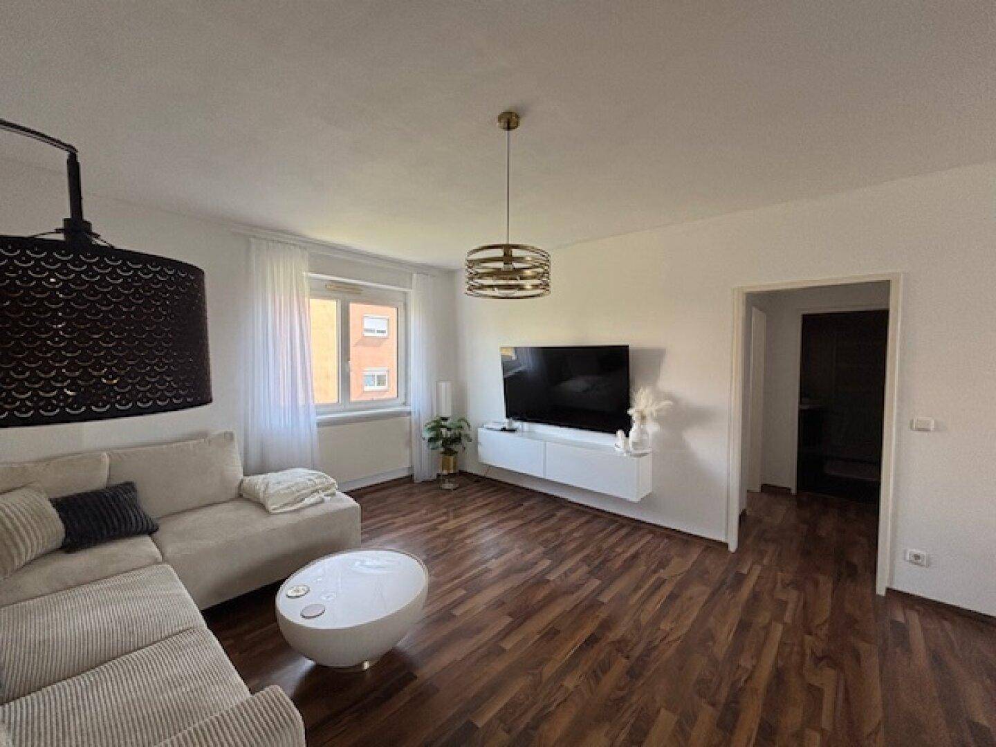 Gemütliches Wohnzimmer mit Ecksofa, Fernseher und dunklem Holzboden.