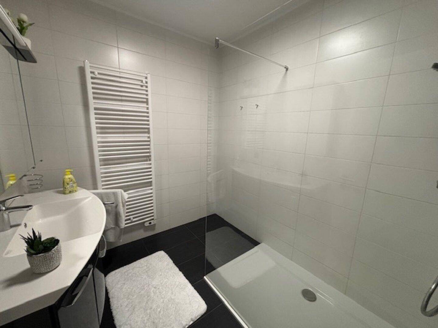 Modernes Badezimmer mit ebenerdiger Dusche, Waschbecken und Handtuchheizkörper.