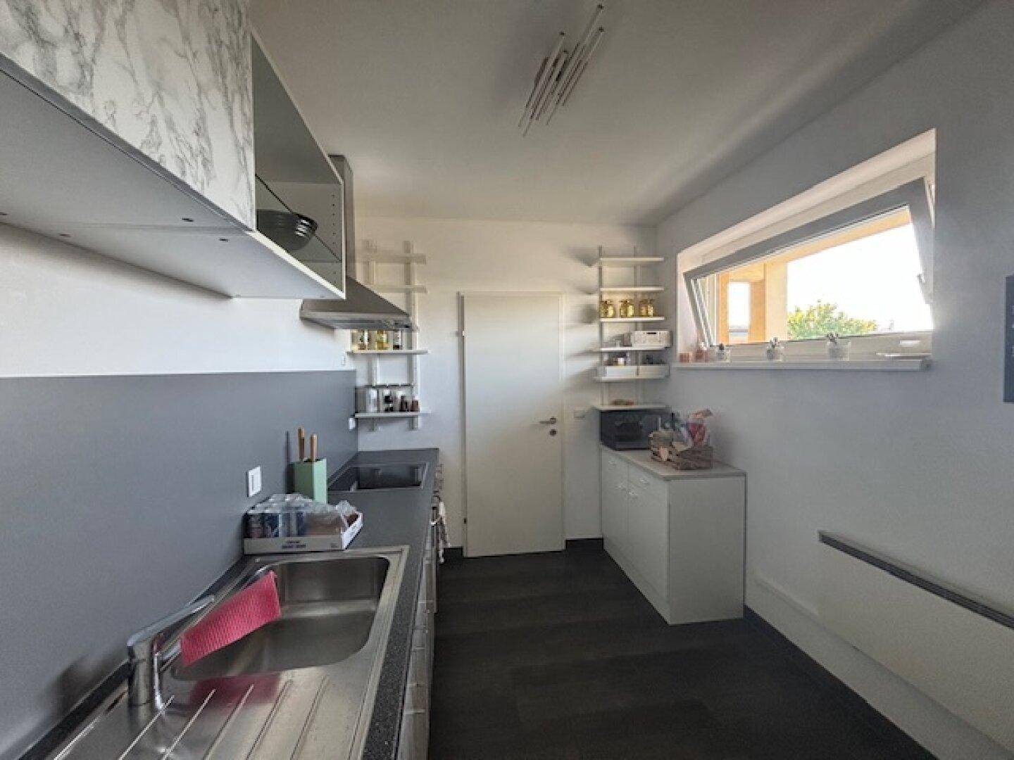Funktionale Küche mit Spülbecken, Oberschränken und Fenster für Tageslicht.