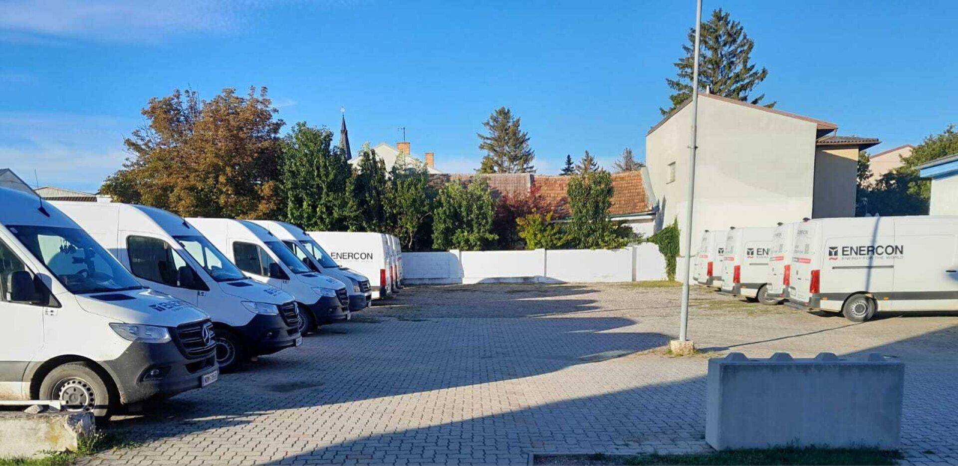 Großer Parkplatz mit einer Reihe von Lieferwagen und einem Gebäude im Hintergrund unter klarem Himmel.