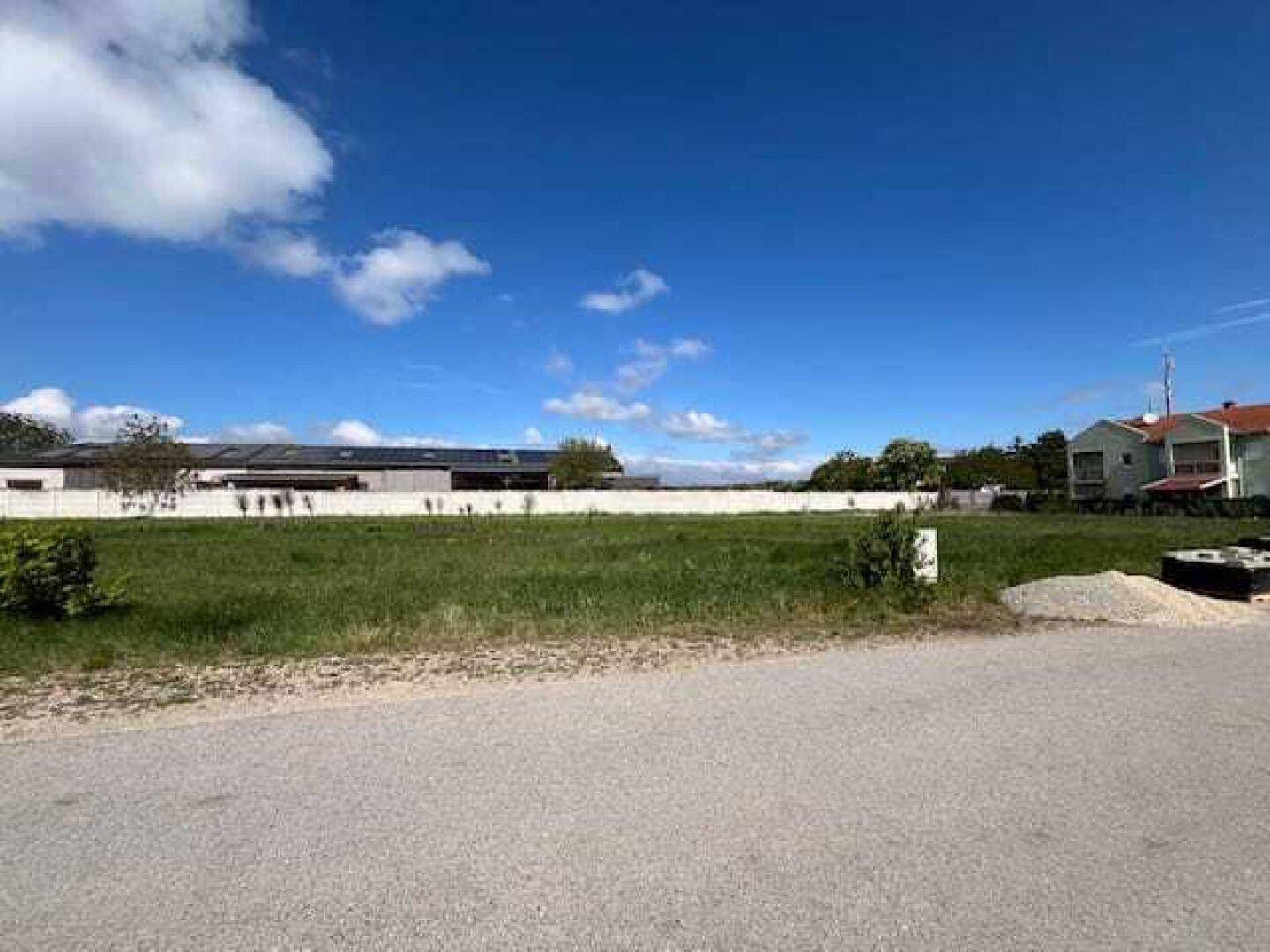 Weitläufiges, unbebautes Grundstück mit grüner Wiese und einem Gebäude mit Solaranlage im Hintergrund.