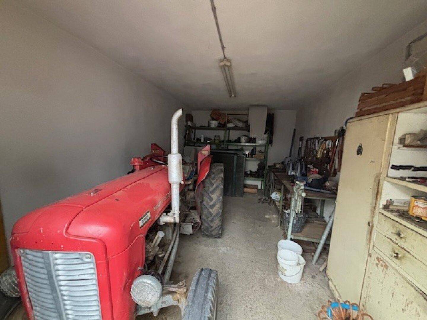 Garage oder Werkstatt mit einem roten Traktor und Regalen für Werkzeuge und Materialien.