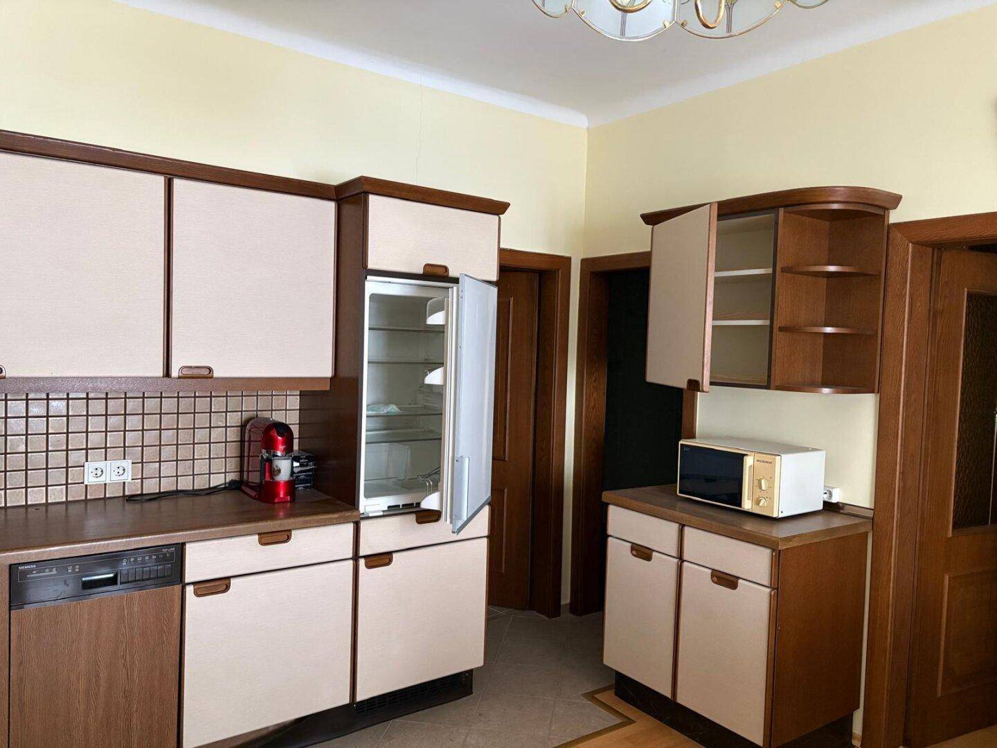 Klassische Küche mit hellen Fronten, Holzelementen und integriertem Kühlschrank, Mikrowelle und Spülmaschine.