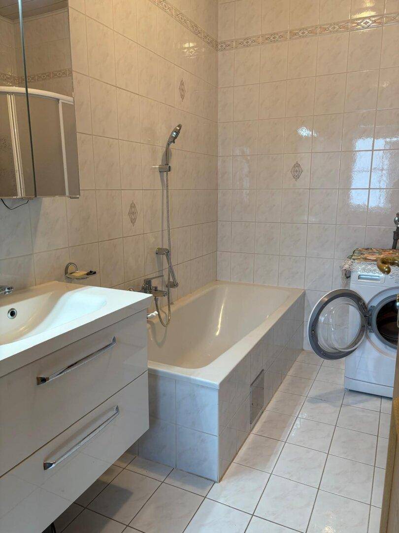 Helles Badezimmer mit Badewanne, Waschbecken, Spiegelschrank und einer Waschmaschine.