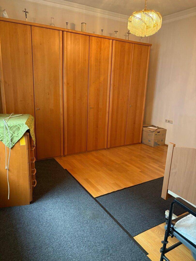 Schlafzimmer mit großem Holzschrank, Teppichboden und einem Bereich mit Parkettboden.