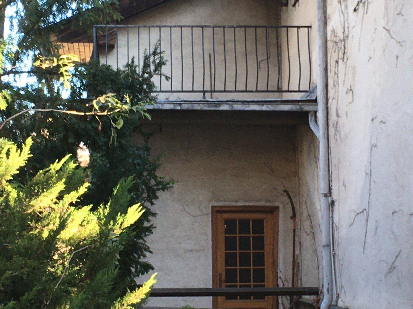 Detailansicht des Balkons mit schmiedeeisernem Geländer und Holztür.