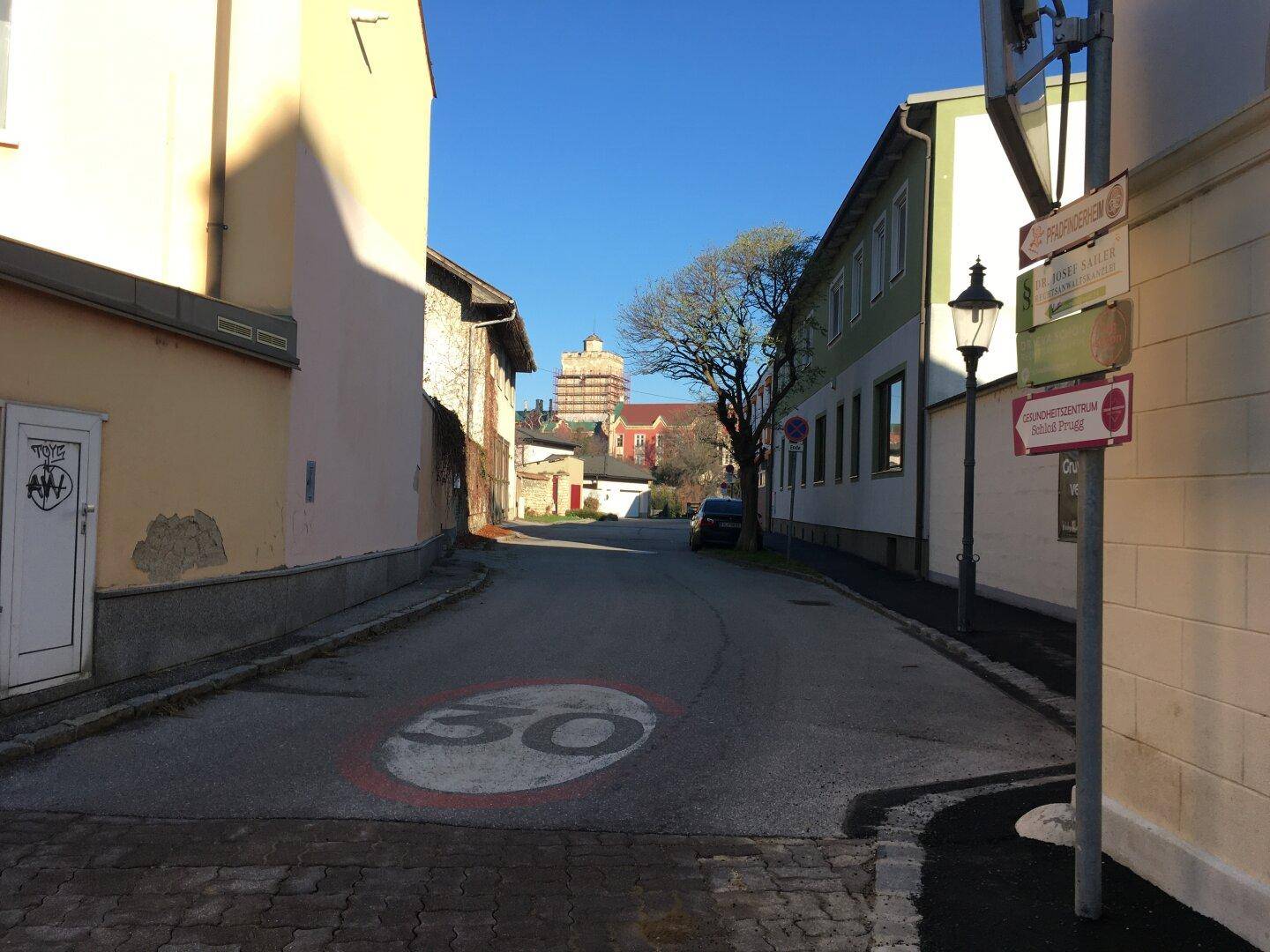 Ruhige Wohnstraße mit Gebäuden und einem 30 km/h Geschwindigkeitsschild auf dem Asphalt.