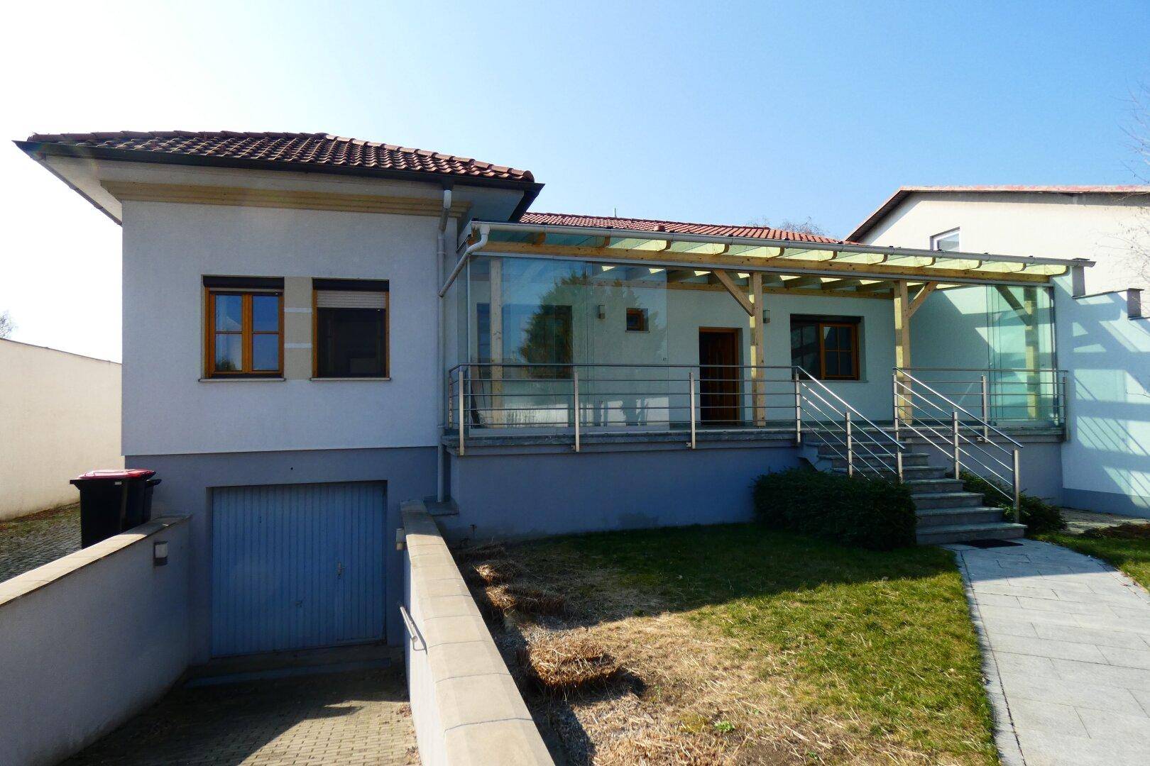 Modernes Haus mit überdachter Terrasse, Garage im Untergeschoss und Garten.
