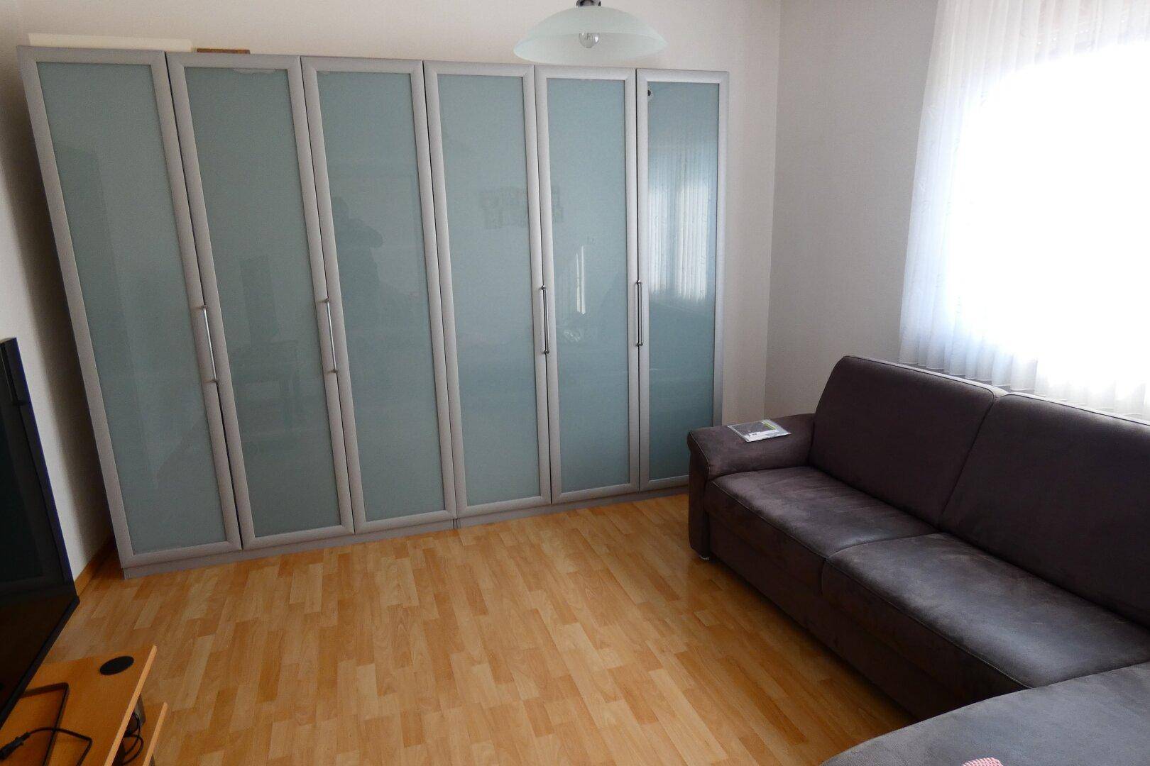 Schlafzimmer mit großem Kleiderschrank, Sofa und hellem Laminatboden.