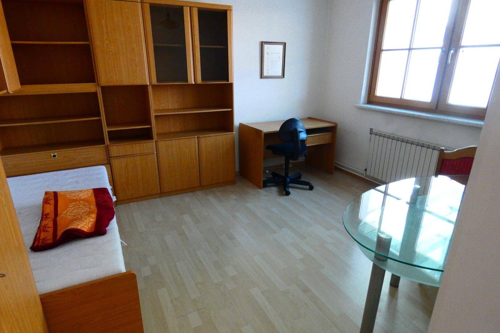 Helles Arbeitszimmer mit Holzregalen, Schreibtisch und einem Fenster mit Blick nach draußen.