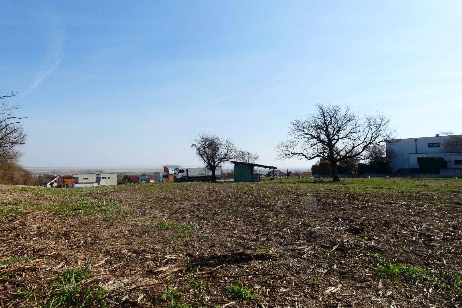 Offenes Gelände mit Blick auf entfernte Gebäude, Lastwagen und eine weite Landschaft unter klarem Himmel.