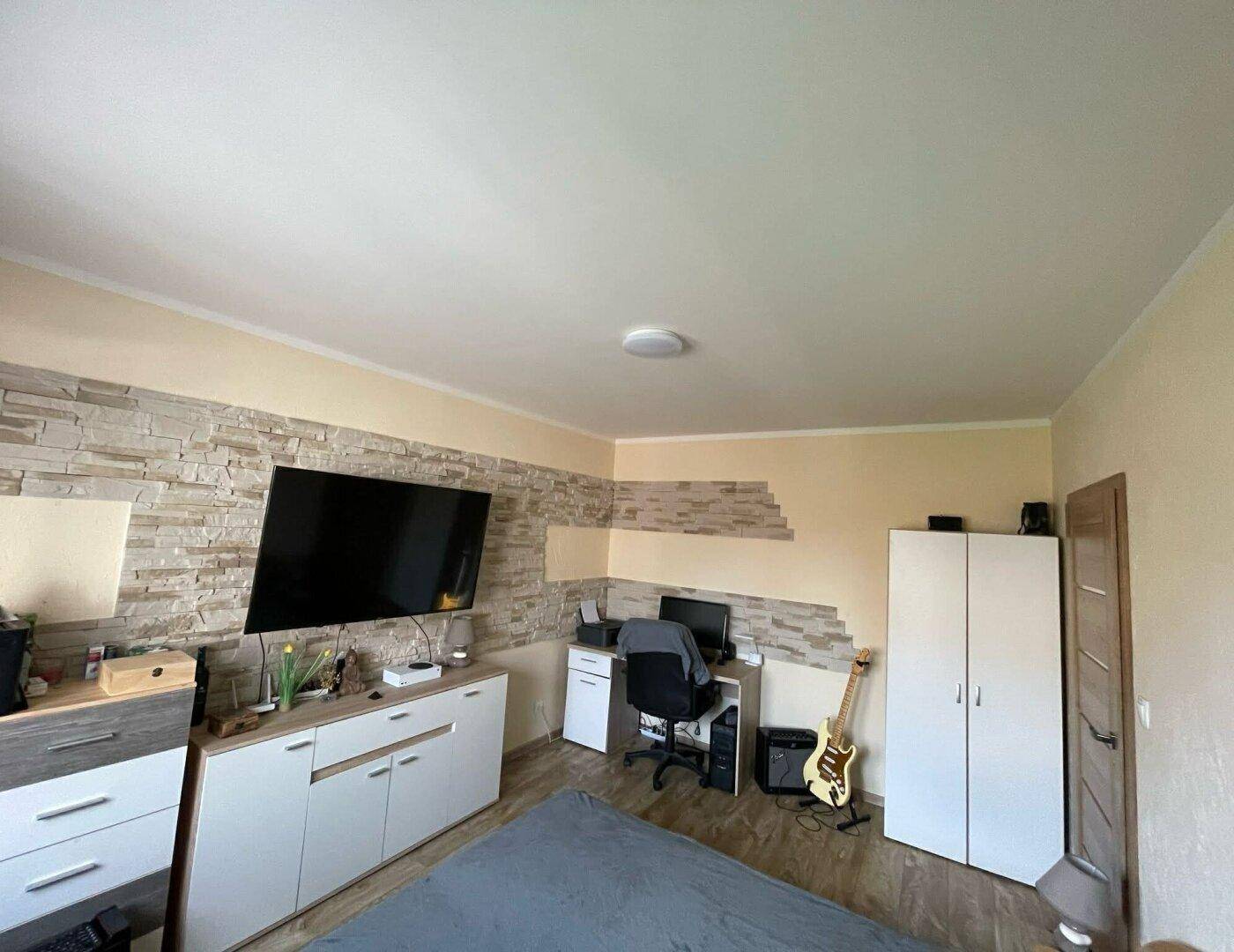 Helles Schlafzimmer mit Arbeitsbereich, Kleiderschrank und dekorativer Steinwand.