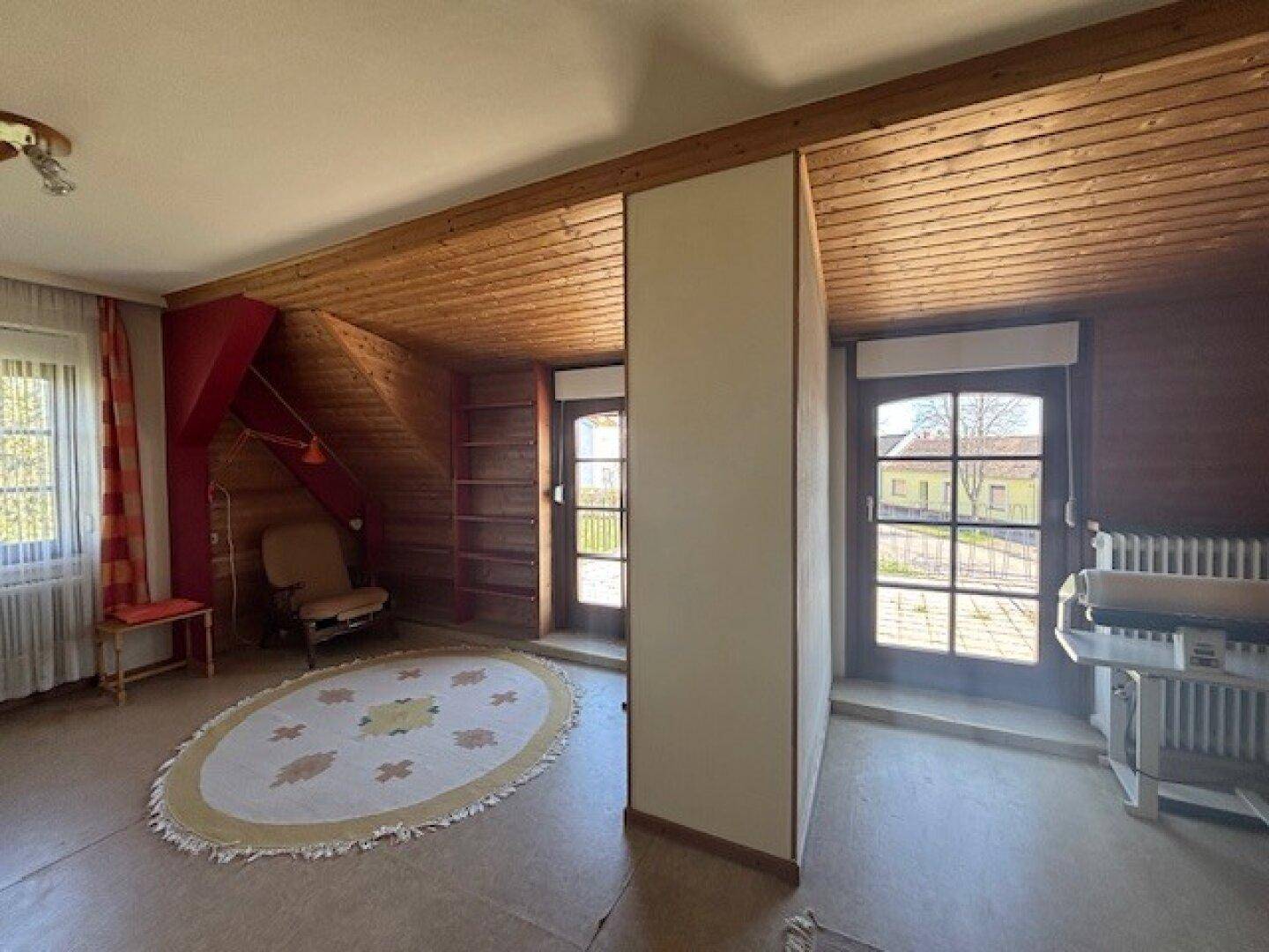 Dachzimmer mit Holzdecke, Vinylboden und Zugang zu einem kleinen Balkon.