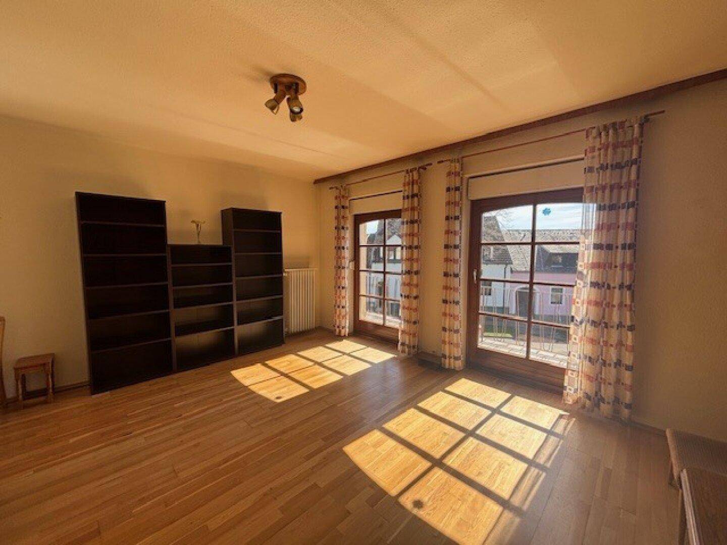 Sonniges Zimmer mit Parkettboden, großen Fenstern und Blick auf die Umgebung.
