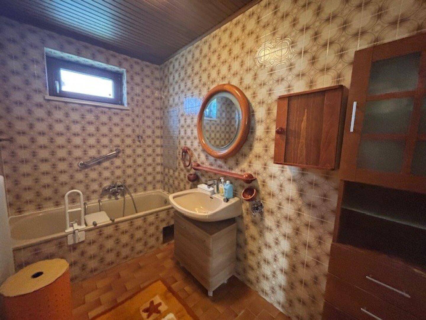 Badezimmer im Stil der 80er Jahre mit gemusterten Fliesen, Badewanne und Fenster.