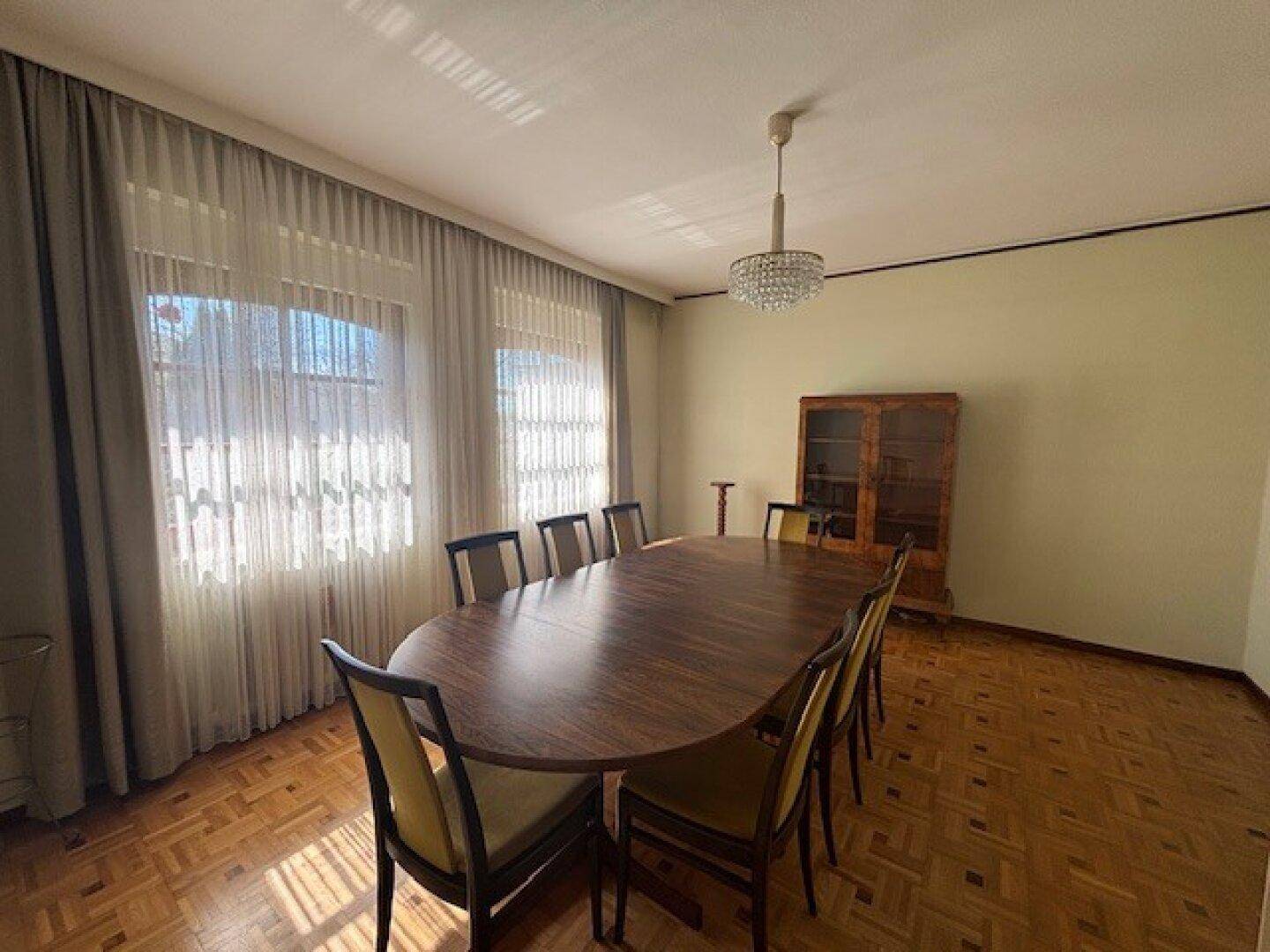 Elegantes Esszimmer mit großem Holztisch, passenden Stühlen und Kronleuchter.