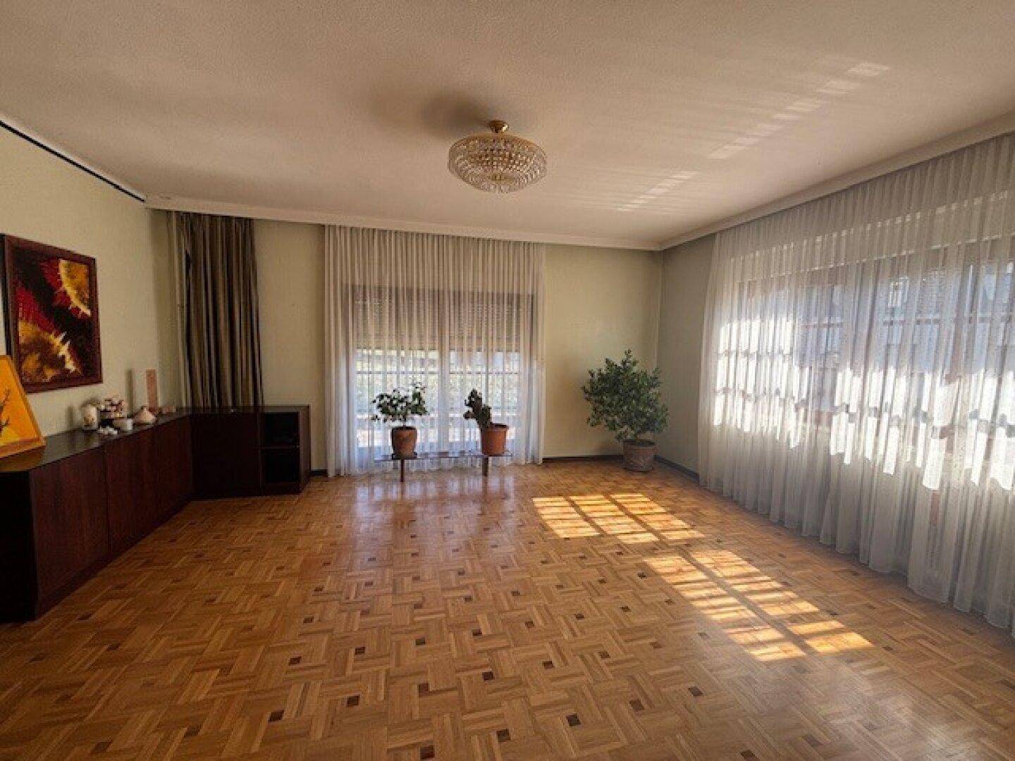 Geräumiges Wohnzimmer mit Parkettboden, großen Fenstern und viel natürlichem Licht.