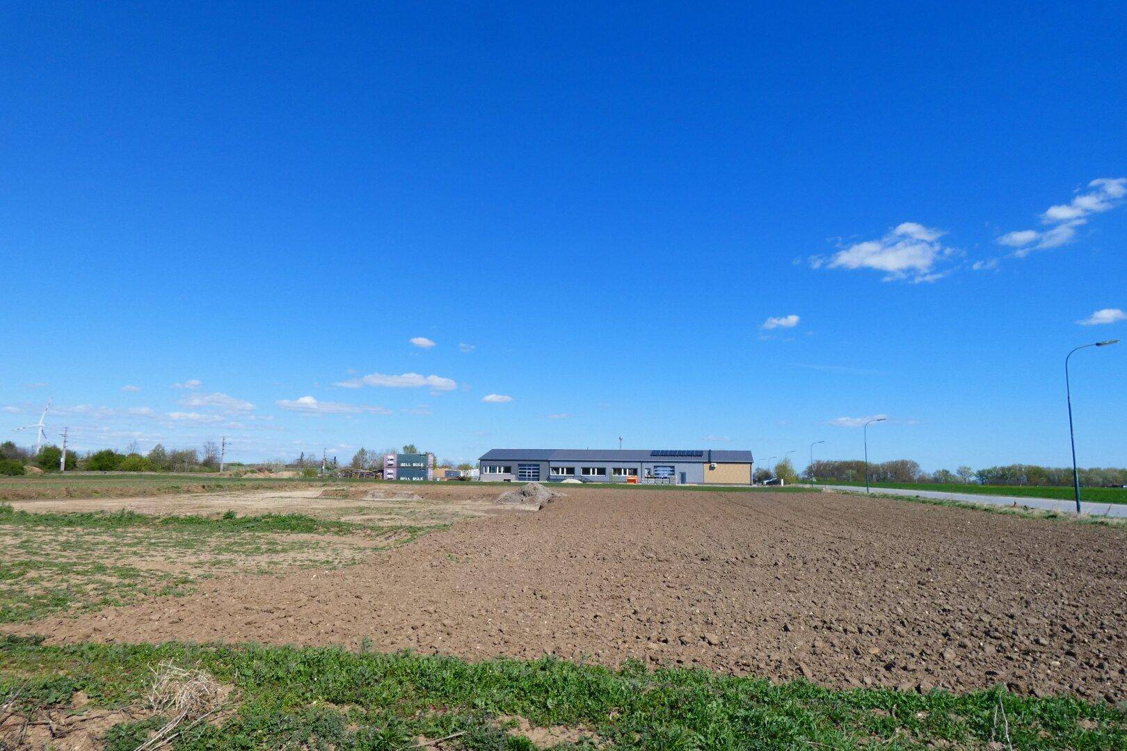 Ackerland im Vordergrund mit einem modernen Gebäude und einer Straße in der Ferne unter blauem Himmel.
