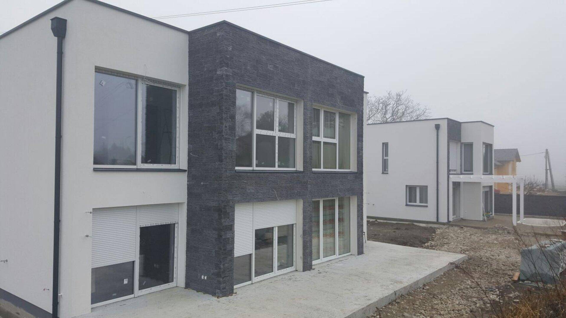 Neubau-Doppelhaushälfte mit moderner Fassade und Rollläden in nebliger Umgebung.