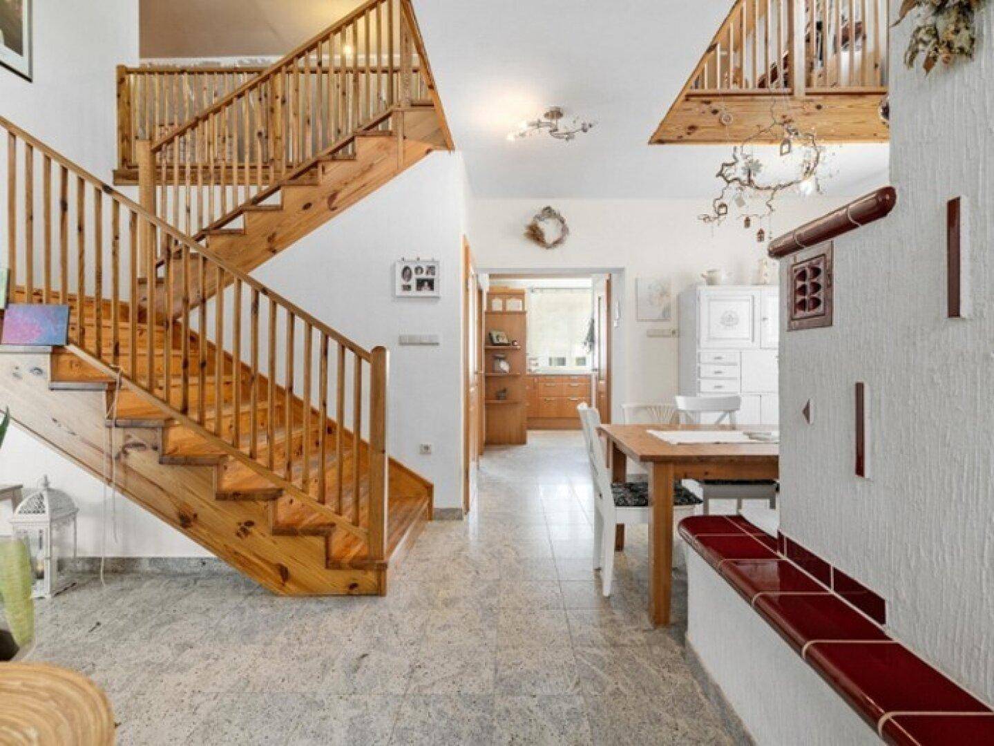 Heller Eingangsbereich mit Holztreppe, Fliesenboden und traditionellem Kachelofen.