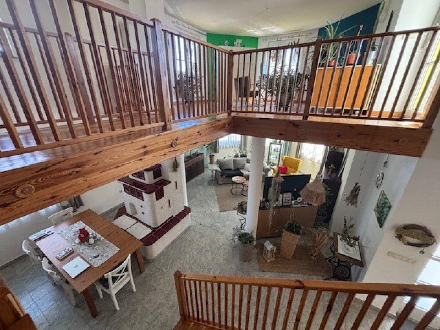 Weitläufiger Wohnbereich mit offener Holztreppe, Galerie und traditionellem Kachelofen.